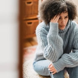 Woman sitting on the floor rubbing her temple.
