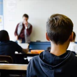 Students listening to a teacher in a classroom setting.