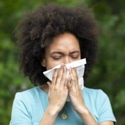 Woman experiencing allergies or sinus pressure blowing her nose with a tissue.