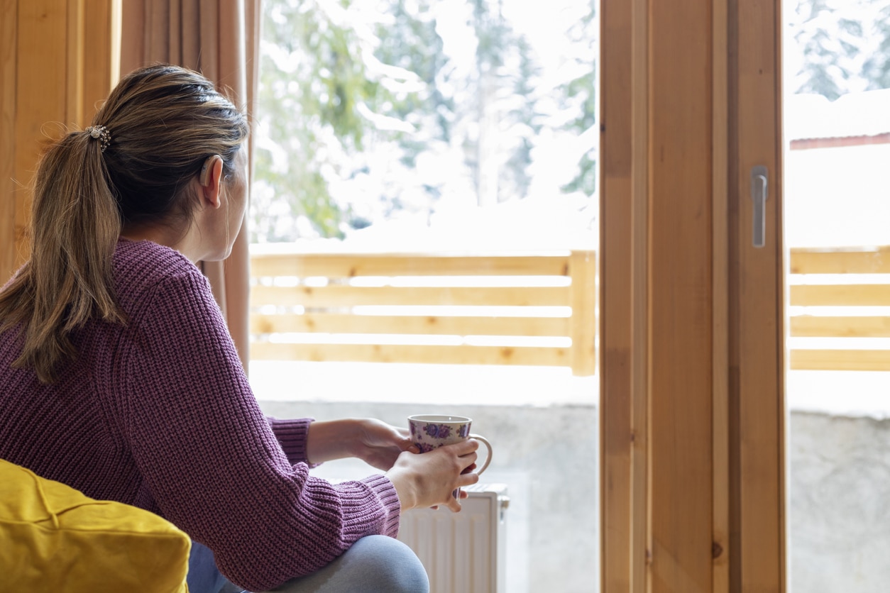 Woman with a hearing aid looking out a snowy window.