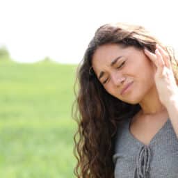 Woman in field with tinnitus holds ear