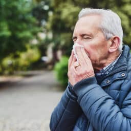 Man in a jacket blowing his nose in the park