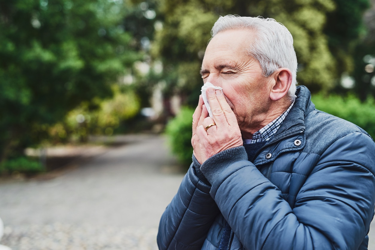 Man in a jacket blowing his nose in the park