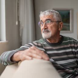 Contemplative older man sitting on his couch at home looking out the window.