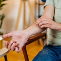 Mid-adult man having a rash (skin condition) while sitting in an armchair at home. Scratching his skin. Close-up.